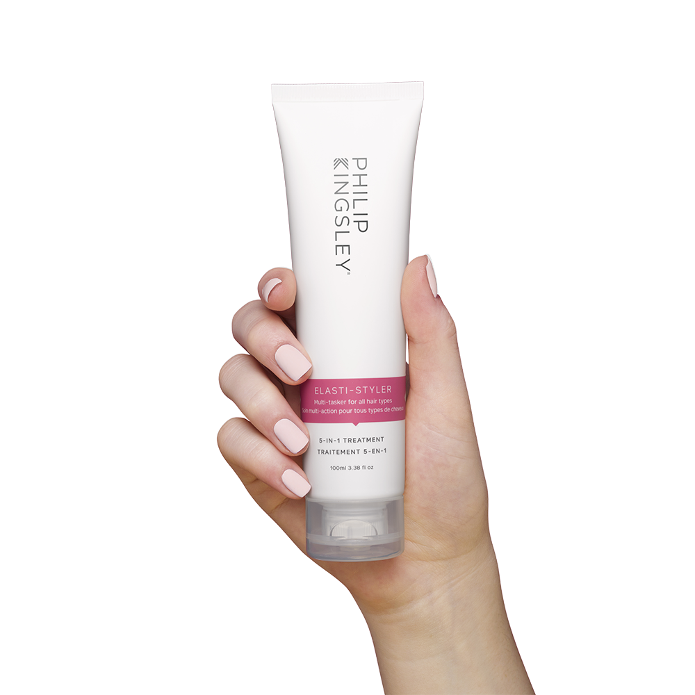 Hand holding the Philip Kingsley elasti-styler 5-in-1 treatment. Achieve shiny, smooth hair with our anti-frizz & conditioning serum.